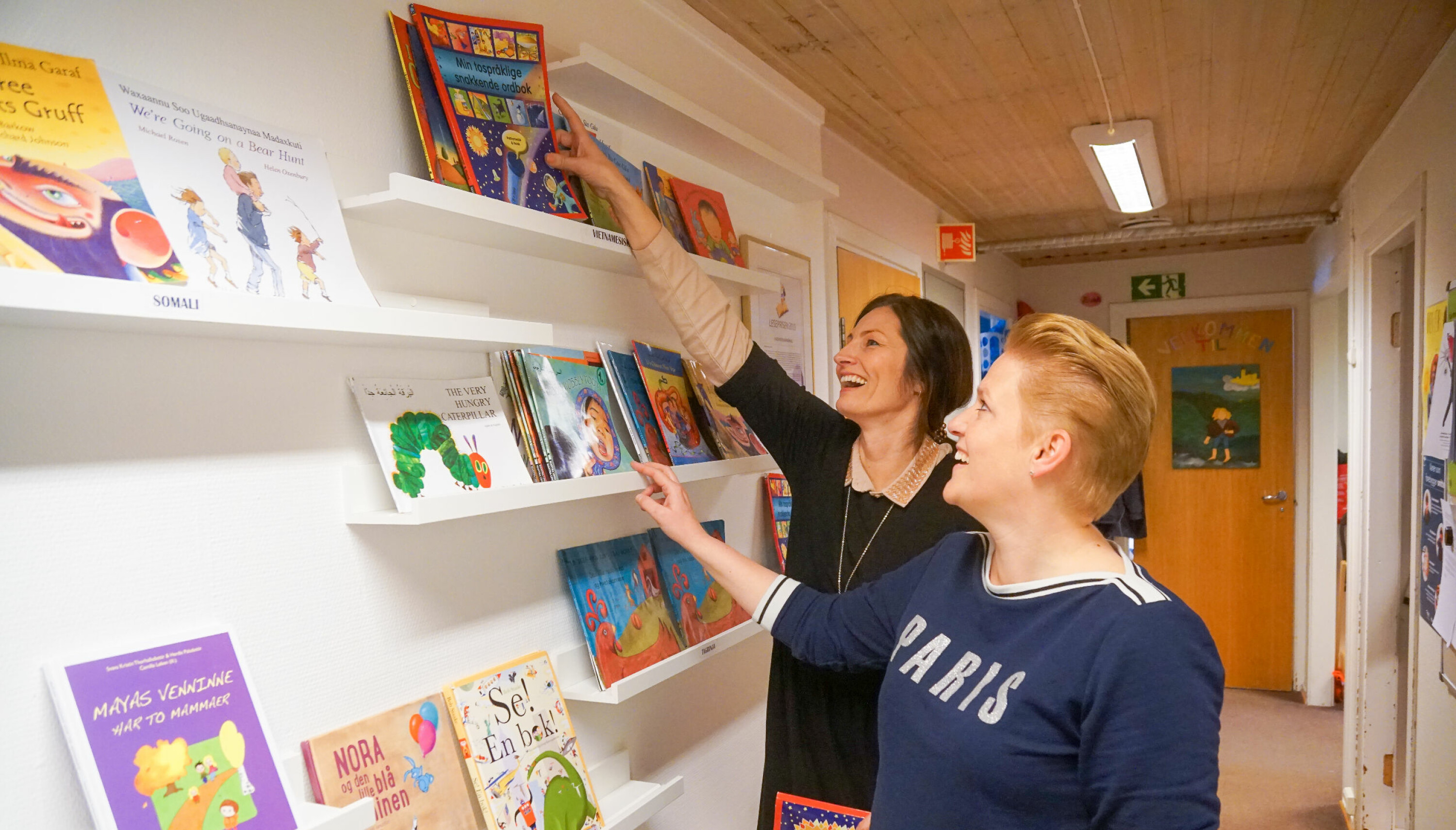 Heidi Cecilie Gilje (t.h) og Trine Hoftvedt viser fram biblioteket de har bygget opp med bøker på mange ulike morsmål. Foreldre kan låne med bøker hjem.
