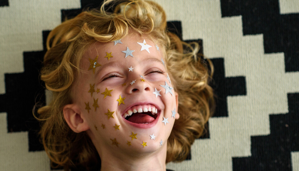 A cute young boy with curly hair laughing while having star-shaped stickers on his face