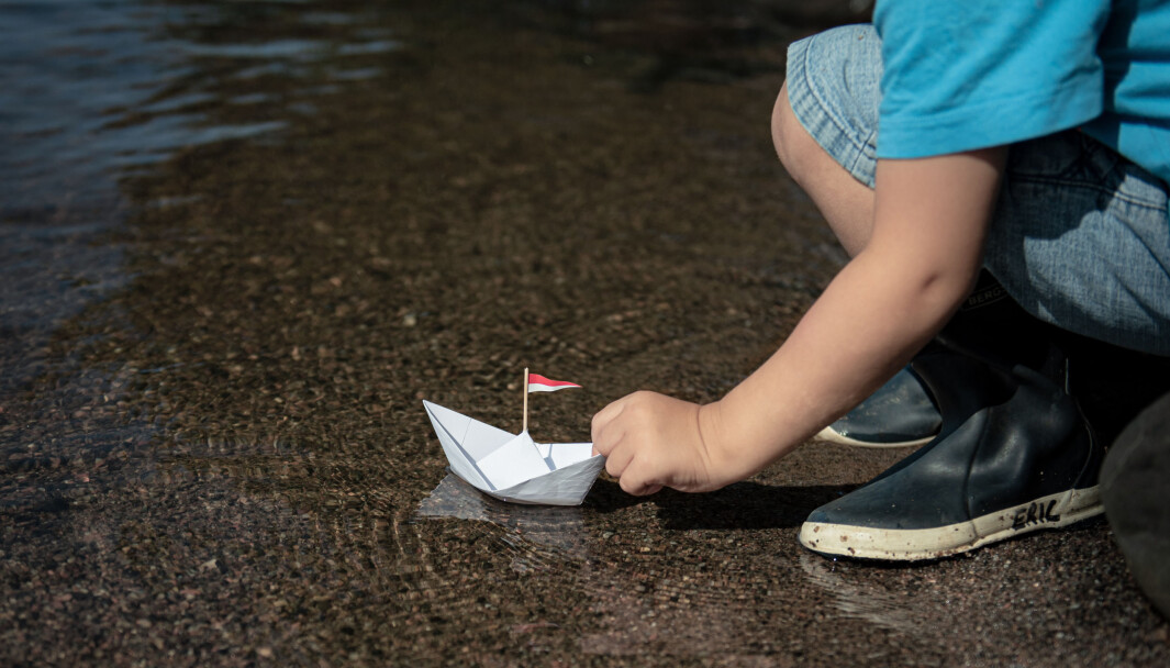 Kleiner Junge setzt Papierschiff ins Wasser Kleiner Junge setzt Papierschiff ins Wasser