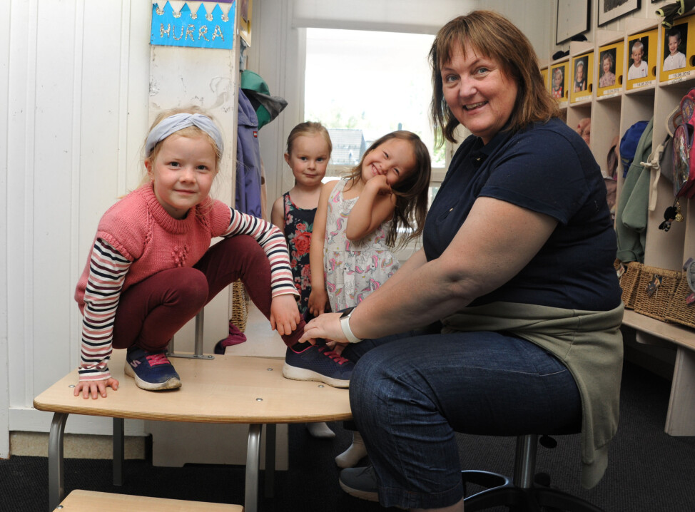 Pedagogisk leder Mona Thorsen sitter på en påkledningsbenk og veileder barna Rikka Othelie Abelquist (t.v.), Mie Emilie Tran-Holm og Emma Helene Alfsen Drage til å ta på seg skoene. Da slipper hun å bøye seg eller sitte på kne.