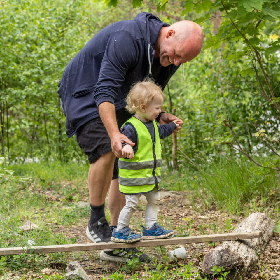 Tobias Lillehagen (1) øver på balanse på en planke i skogen med god støtte fra pedagogisk leder Espen Øby.