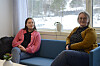 To kvinner sit i ein blå sofa på Hjelteryggen skole med vinterlandskap synleg gjennom vindauget bak.