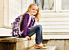 Jente ca. 6-7 år sitter på trapp hjemme med skolesekken på.