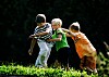 Tre gutter leker ute på en grønn plen i sommersol.