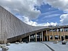 Moderne bygning med skrå fasade, søyler og steiner på en åpen plass.