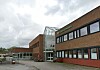 Mursteinsbygning med store vinduer og glassinngang ved en tom skolegård.
