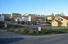 Utsikt over bygninger, boliger og en vei i et stille nabolag under blå himmel.