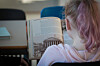 Barn med rosa hår leser i en bok i et klasserom.