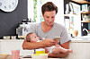 Far holder en baby og ser på mobilen ved kjøkkenbenken.