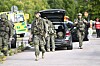 Bevæpnet politi og beredskapspersonell ved Brinellskolan, med ambulanse og utrykningskjøretøy i bakgrunnen.