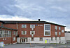 Rød mursteinsskole med store vinduer og skolegård under en overskyet himmel.