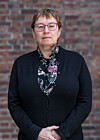 Portrett av en kvinne med briller foran en rød murvegg.