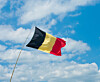 Belgiske flagget vaier mot blå himmel og hvite skyer.