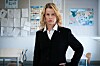 Kvinne i svart blazer står foran oppslagstavler i et klasserom.