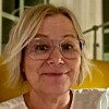 Nærbilde av en kvinne med lyst hår og briller foran en gul sofa.