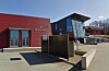 Moderne næringsbygg med rød fasade, glassinngang og åpen plass.